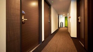 Een hotelgang met houten deuren, tapijtvloeren en een groene wand aan het einde.