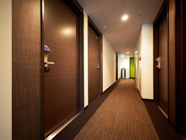 Ein Hotelgang mit Holztüren, Teppichböden und einer grünen Wand am Ende.
