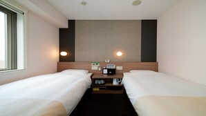 Ein Hotelzimmer mit zwei Einzelbetten, einem Holz-Kopfteil, einem kleinen Nachttisch mit Telefon und Kaffeemaschine sowie einer wandmontierten Leuchte.