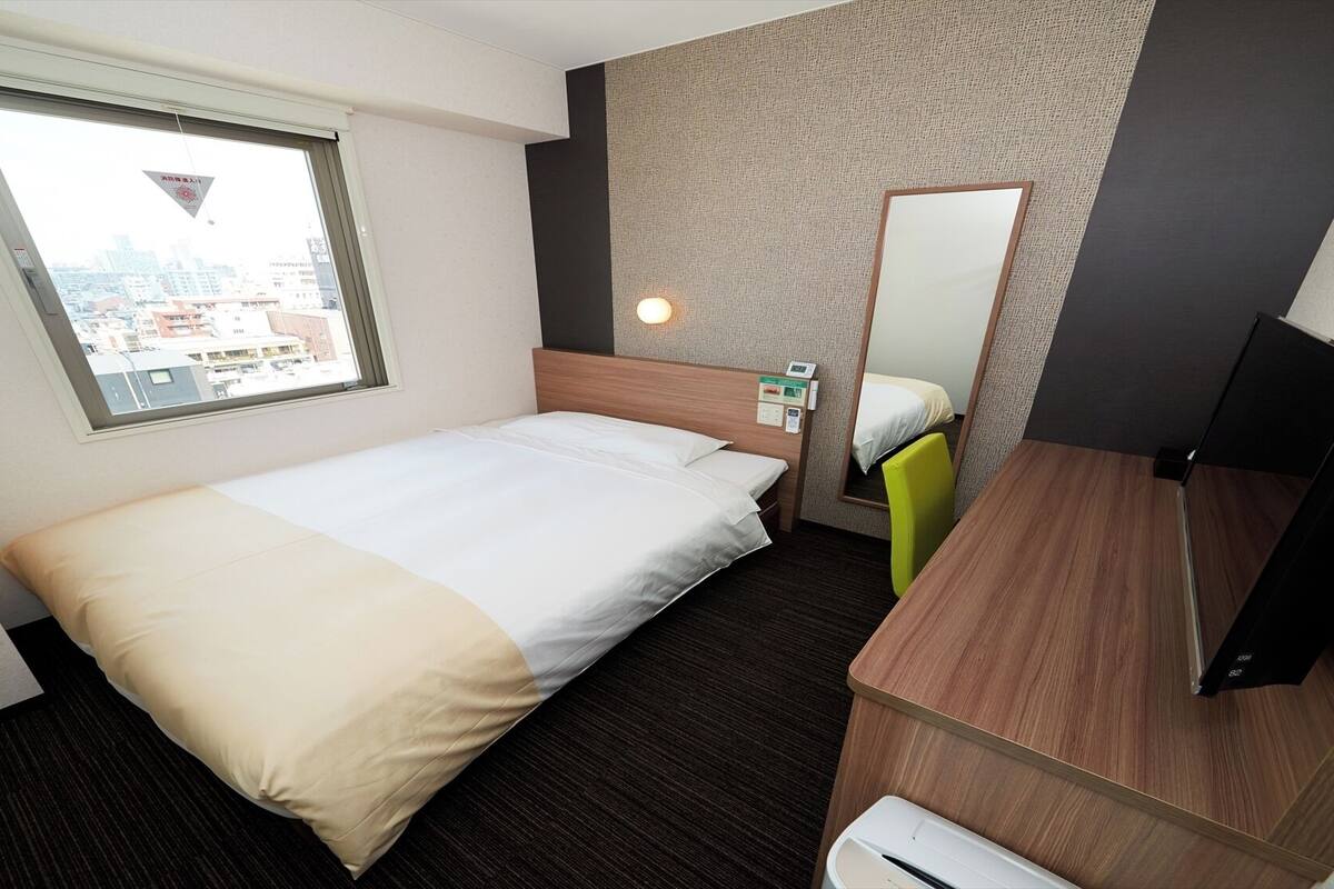Une chambre d’hôtel avec un lit, un bureau, un miroir et une fenêtre donnant sur la ville.
