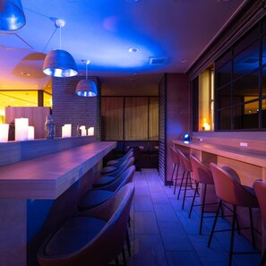 Un espace bar moderne doté d’un long comptoir, de nombreux tabourets et d’un éclairage suspendu.