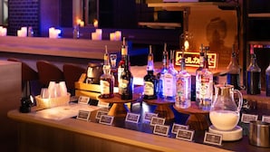 Een bar met diverse drankflessen, een menubord en een sfeervolle achtergrond met kaarsen.