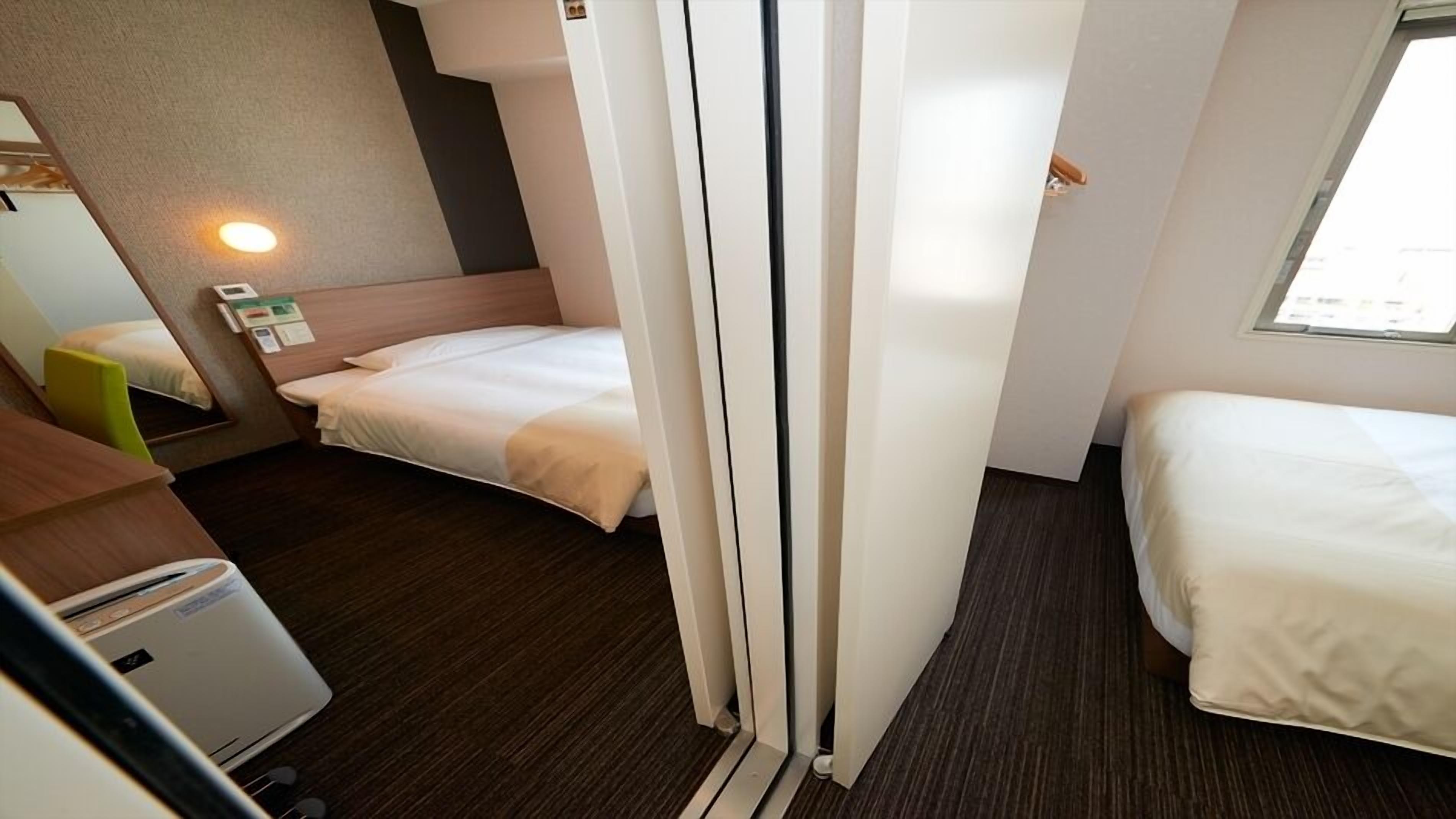 Ein Hotelzimmer mit zwei Betten, einem Schreibtisch, einem Stuhl, einem Heizgerät und einem Fenster.