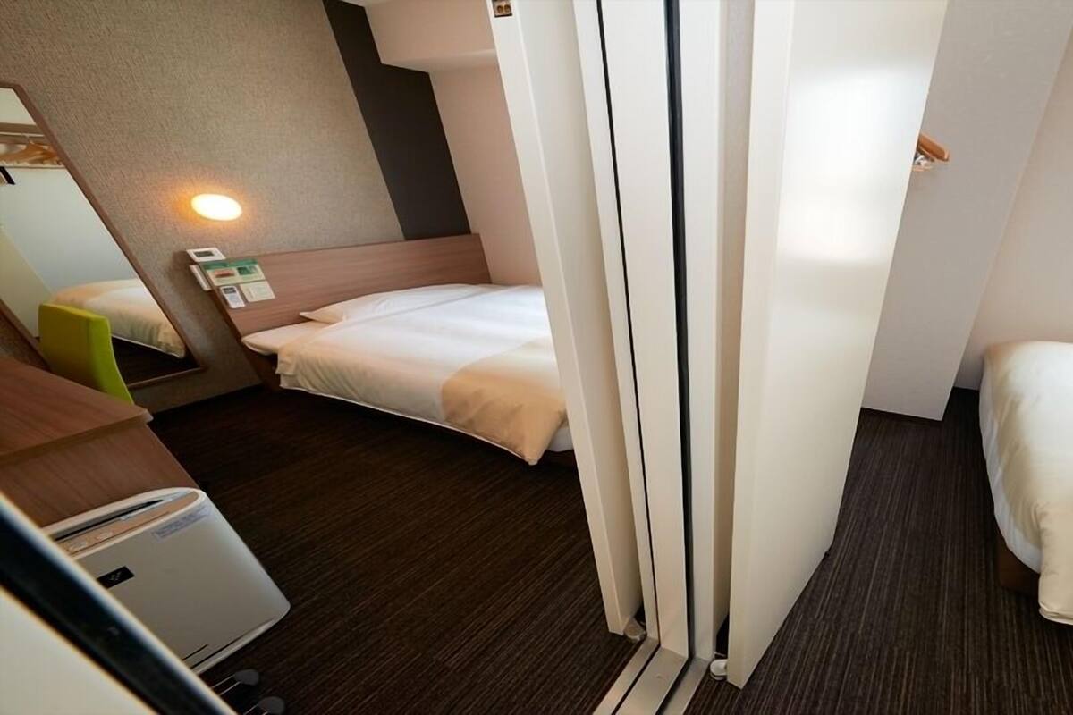 Une chambre d’hôtel avec deux lits, un bureau, une chaise, un radiateur et une fenêtre.