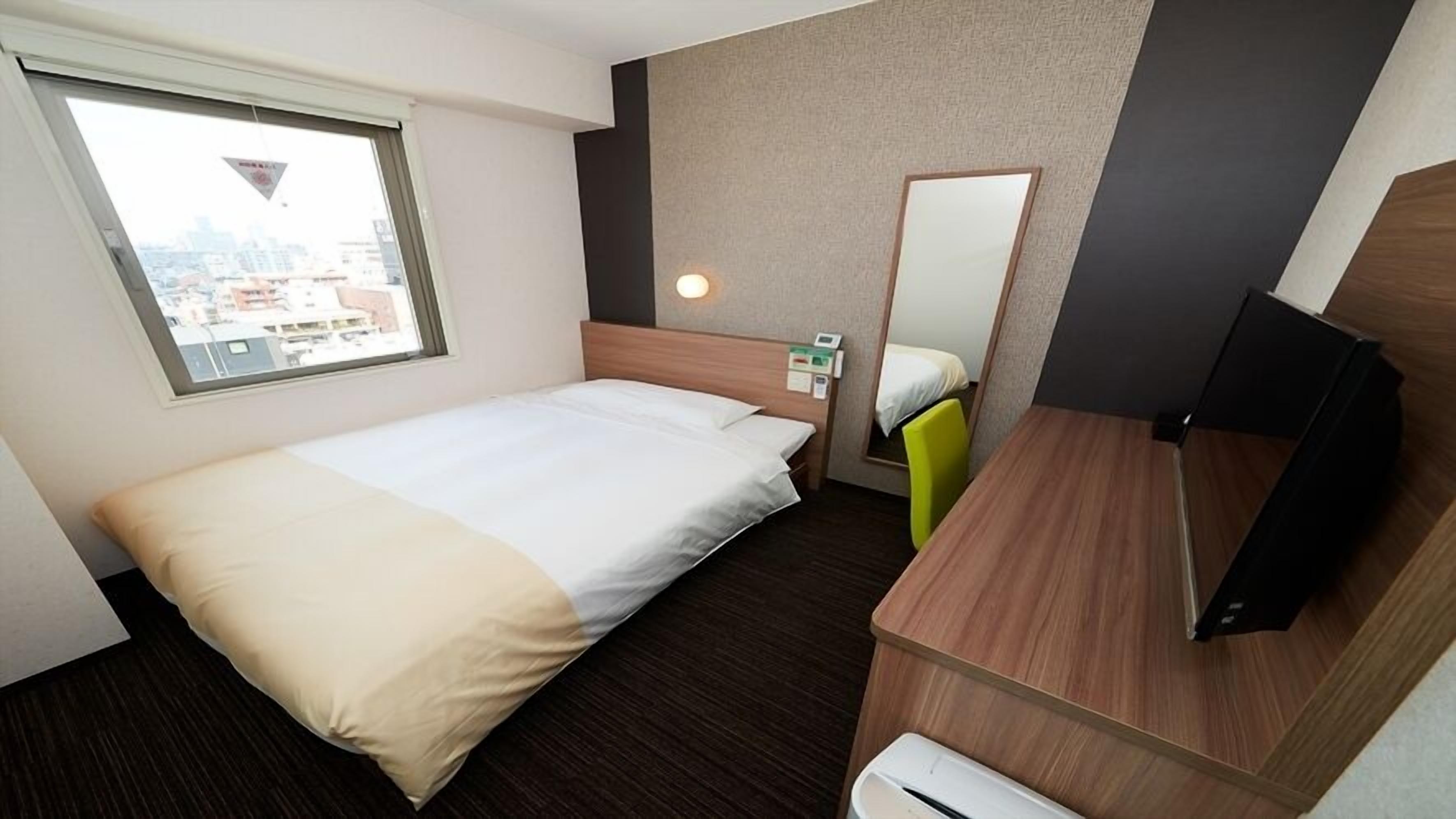 Ein Hotelzimmer mit einem Bett, einem Schreibtisch, einem Stuhl, einem Spiegel und einem Fenster.