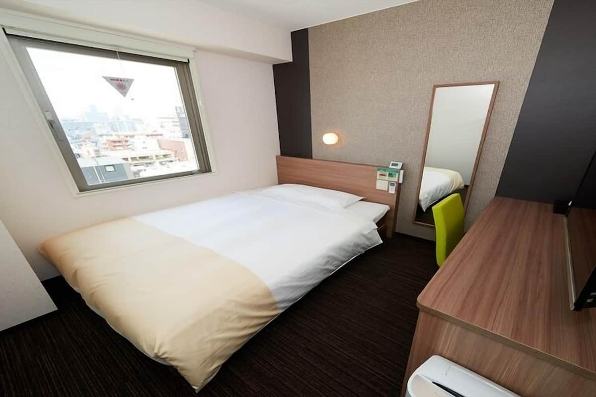 Une chambre d’hôtel avec un lit, un bureau, une chaise, un miroir et une fenêtre.