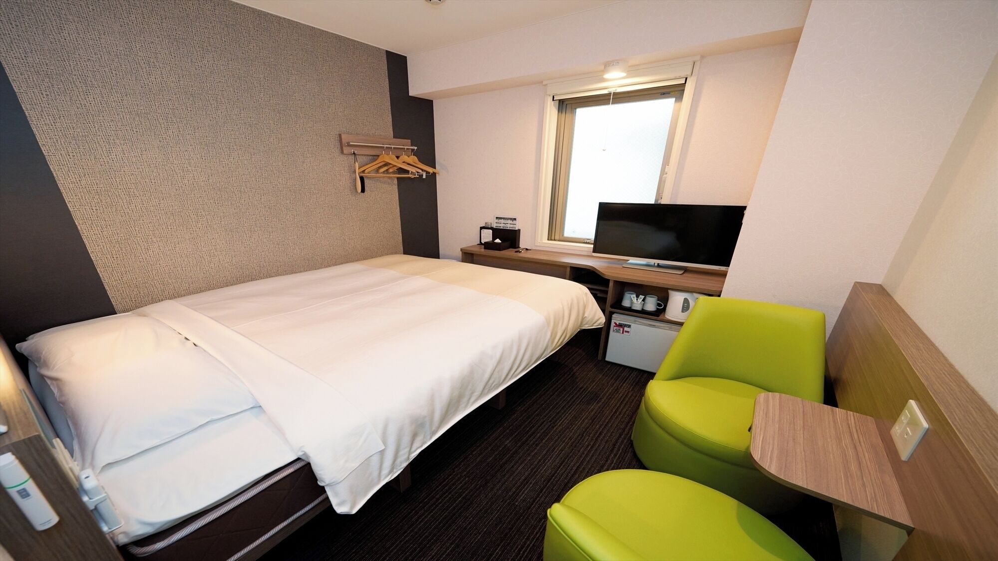 Ein Hotelzimmer mit einem Bett, einem Schreibtisch mit Fernseher, einer kleinen Kühlbox und einem grünen Sessel.
