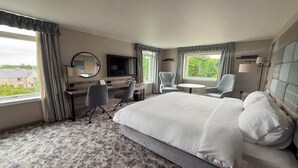 Ett hotellrum med en stor säng, ett skrivbord med en stol, en TV och ett fönster med gardiner.