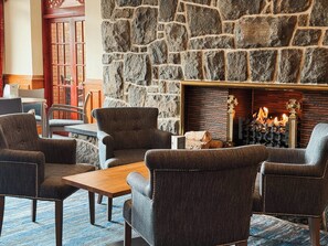 A stone wall, a fireplace with logs, and a seating area with armchairs and a table. - Cabarfeidh Hotel (Stornoway)