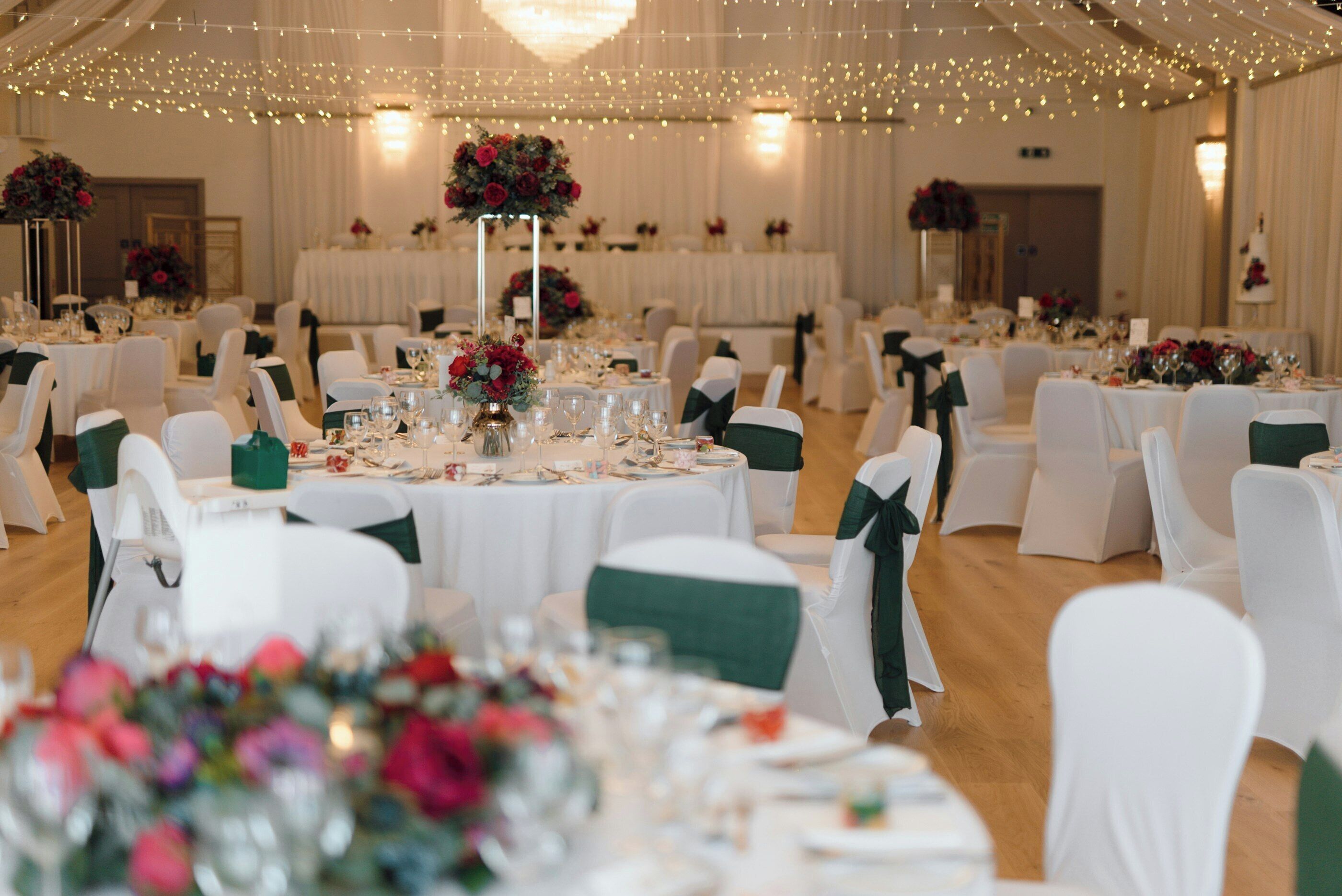 Une salle de banquet avec des tables rondes, des chaises blanches et des centres de table ornés de compositions florales.