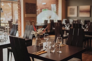 Un'ambientazione da ristorante con tavoli apparecchiati, sedie e un vaso con fiori.