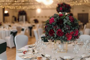 Una mesa de banquete dispuesta con copas de vino, platos y cubiertos, rodeada de sillas blancas con cintas verdes.