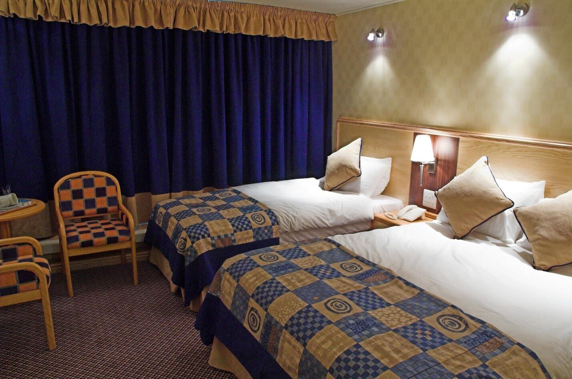 A hotel room with two beds, a chair, a small table, and a lamp.