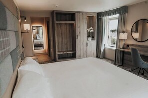 Una habitación de hotel con una cama grande, un escritorio con silla, un armario, un espejo y una ventana con cortinas.