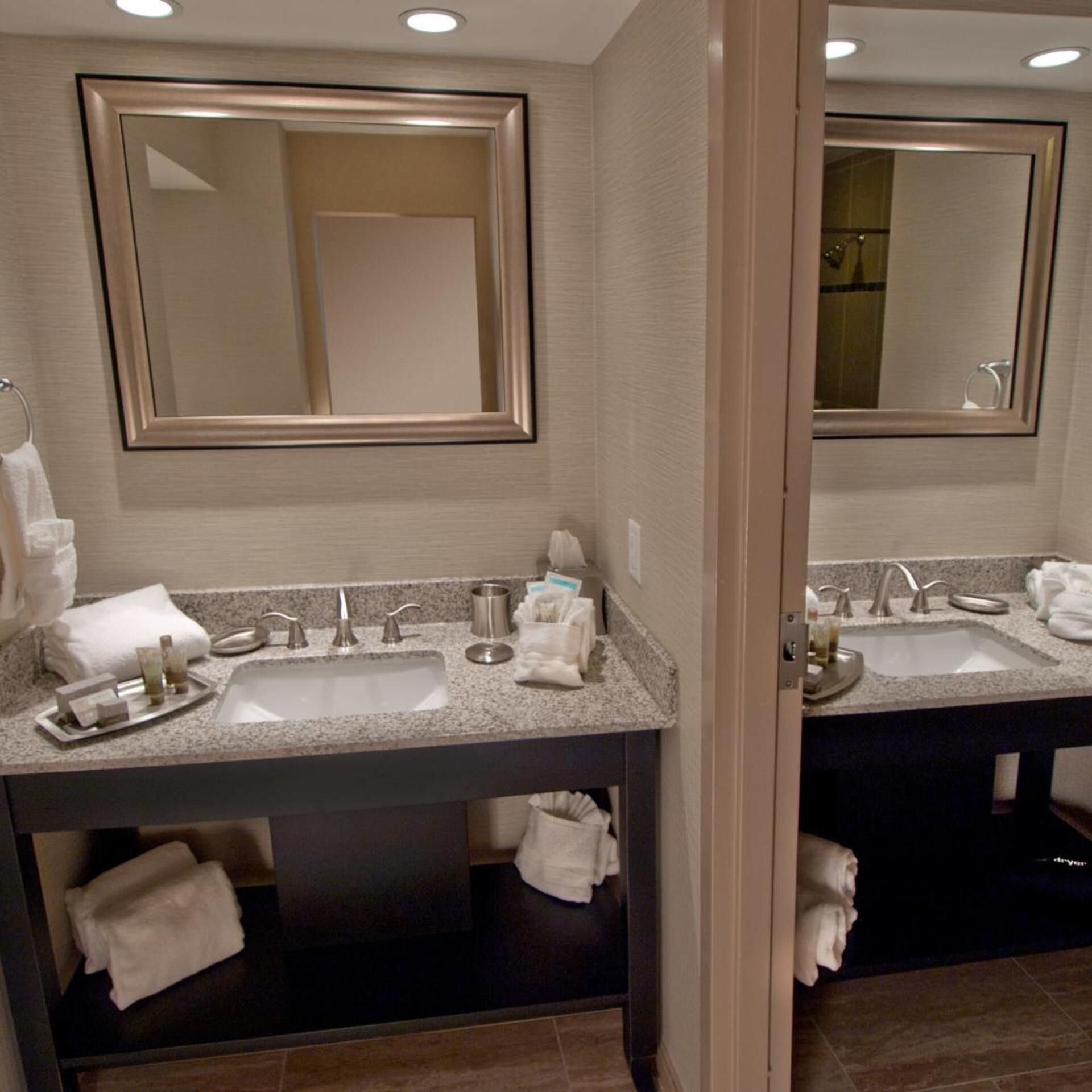 A hotel bathroom with two sinks, a large mirror, and a towel rack.
