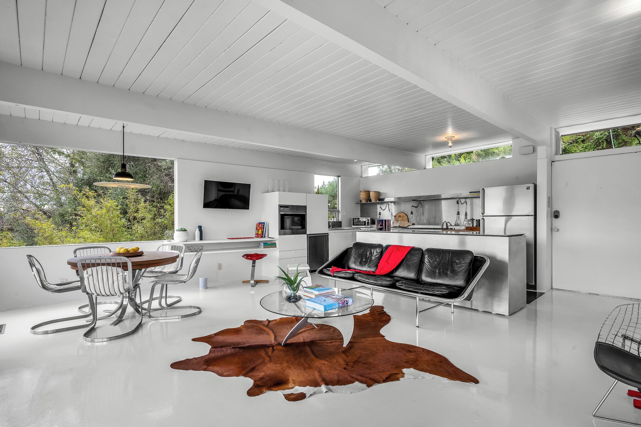 A modern living space with a dining area, a leather sofa, and a kitchen.