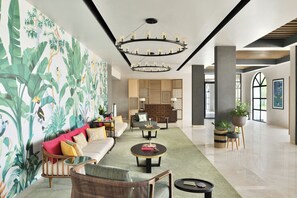 Un hall d’hôtel moderne doté d’un espace salon central, d’un mur décoratif orné de feuillages tropicaux et d’un lustre.