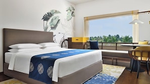 Une chambre d’hôtel moderne, dotée d’un grand lit, d’un bureau et offrant une vue sur la verdure environnante.