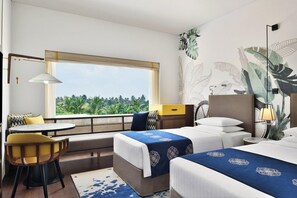 Une chambre d’hôtel avec deux lits, un coin salon avec une table et une grande fenêtre donnant sur des palmiers.