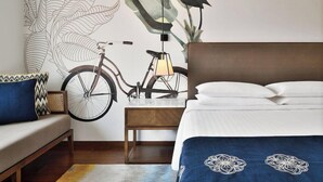 Une chambre avec un grand lit, une table de chevet en bois, un vélo et une fresque murale.