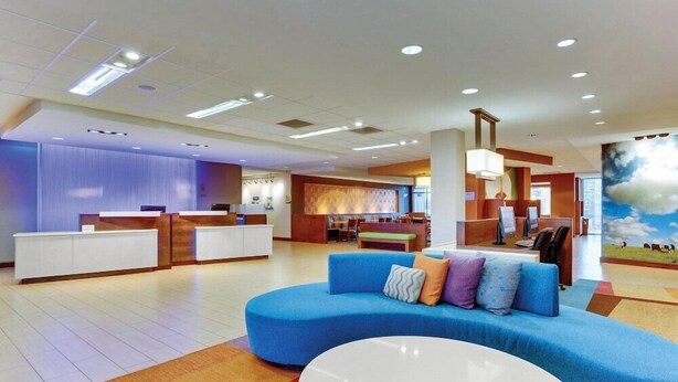 A hotel lobby with a reception desk, a blue sofa, a white coffee table, and a mural on the wall. - Fairfield Inn Suites Dunn I 95 (Dunn)