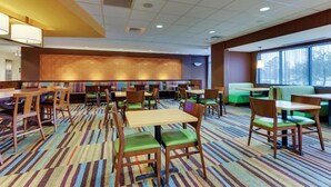 A hotel dining area with multiple tables and chairs, a patterned carpet, and a large window providing natural light. - Fairfield Inn Suites Dunn I 95 (Dunn)