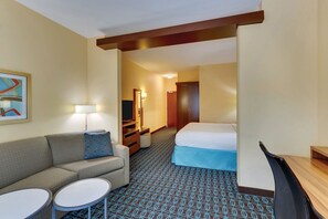 Quarto de hotel com sofá, duas mesinhas, uma cama, televisão, espelho e porta que dá para outro espaço.