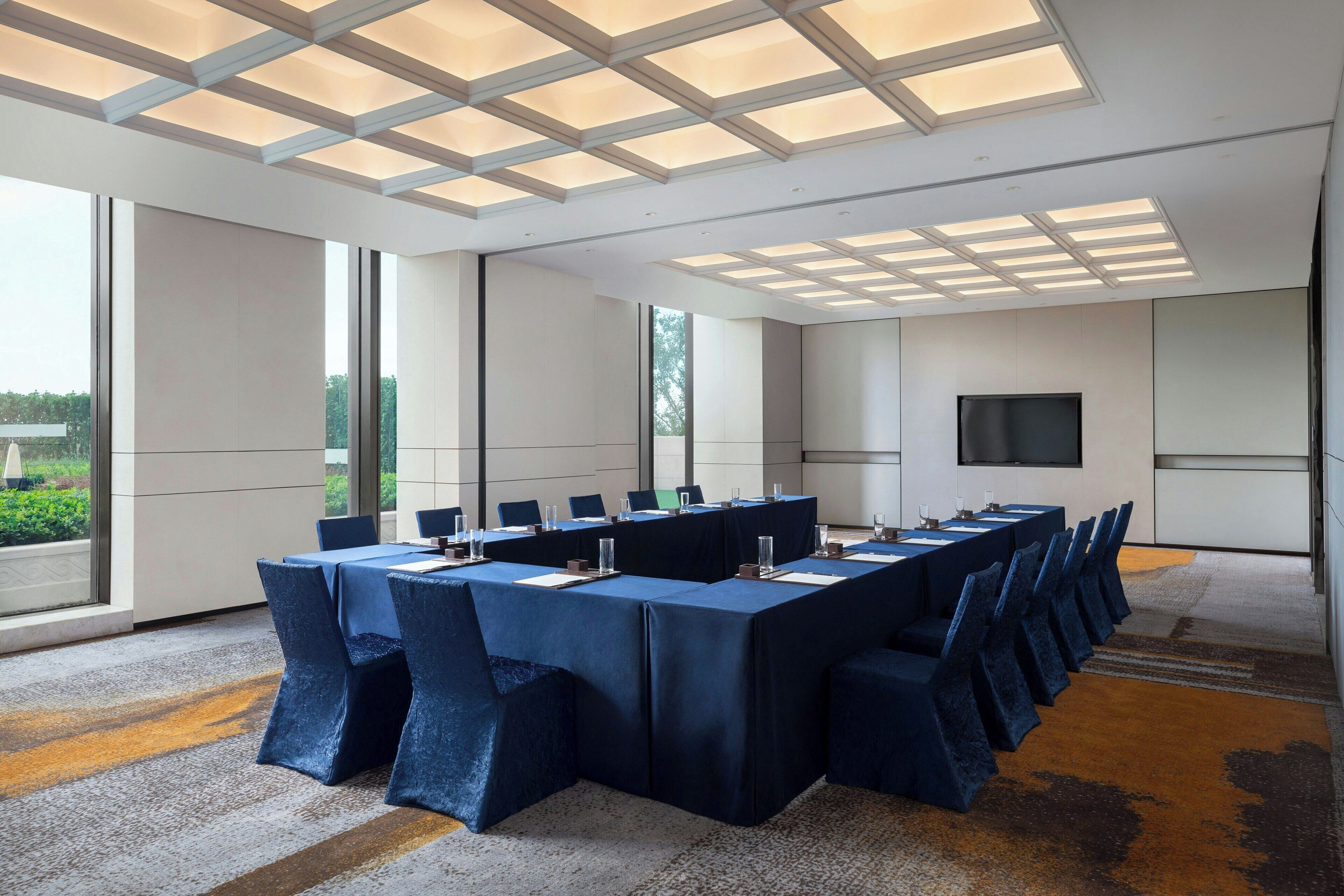 Un salón de conferencias con una mesa larga, sillas y una pantalla de televisión.