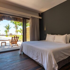 A bedroom with a large bed, a wooden floor, a view of palm trees, and a chair outside. - Blue Holbox (Isla Holbox)