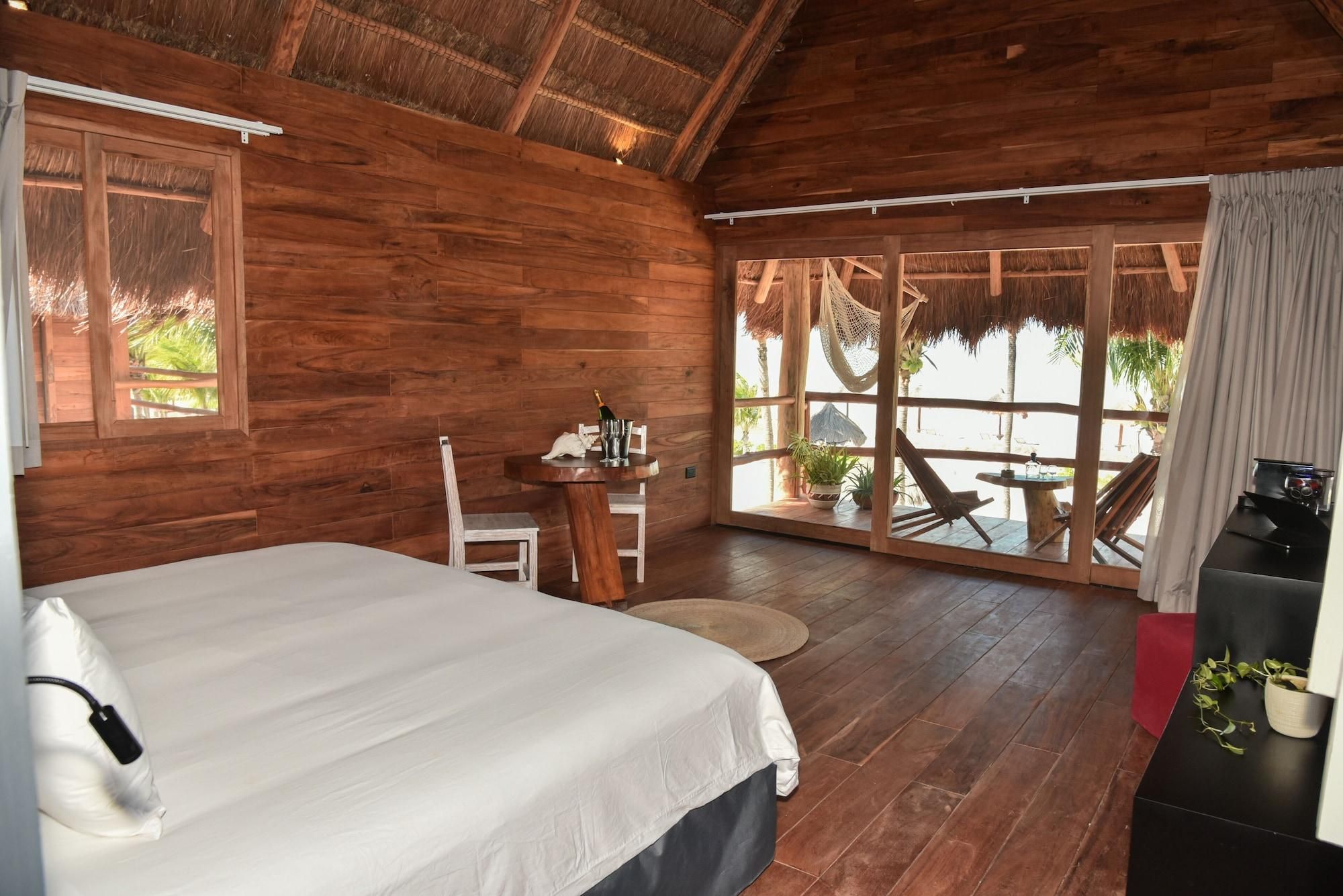 A wooden room with a bed, a table with chairs, and a view of the outdoors.