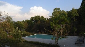A rectangular swimming pool surrounded by lush greenery, with a concrete deck and lounge chairs. - Lebua Corbett (Salt)