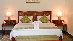 A hotel room with a wooden headboard, two bedside tables with lamps, a bed with white bedding and green pillows, a bench at the foot of the bed, and a framed picture on the wall. - Lebua Corbett (Salt)