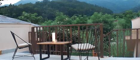 A balcony with a table and two chairs, a candle, and a view of green mountains.