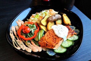 A black plate with grilled salmon, sliced cucumbers, red bell peppers, and a creamy sauce.