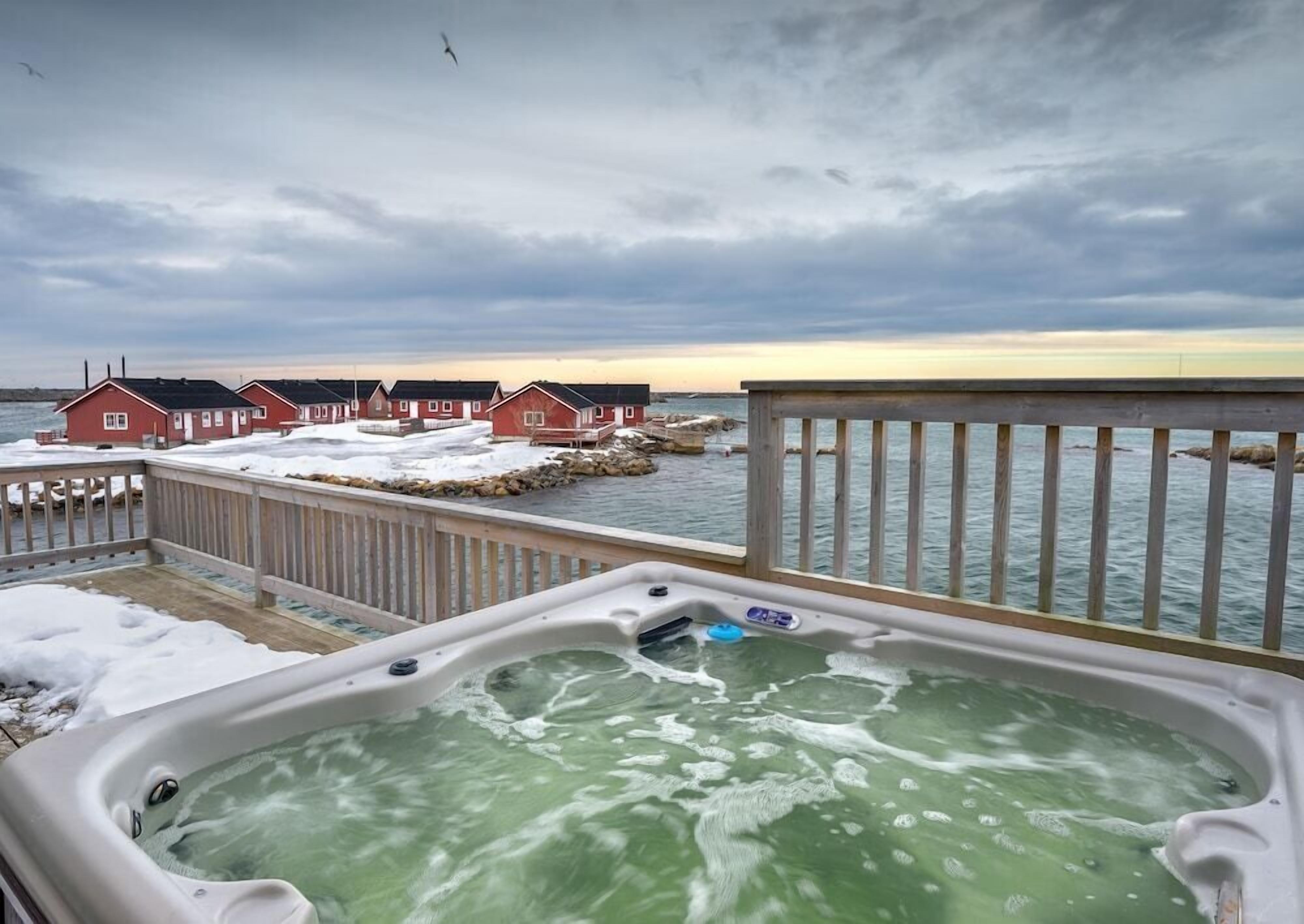 A hot tub on a deck with a view of red houses and a body of water.