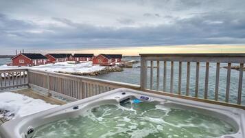 A hot tub on a deck with a view of red houses and a body of water.