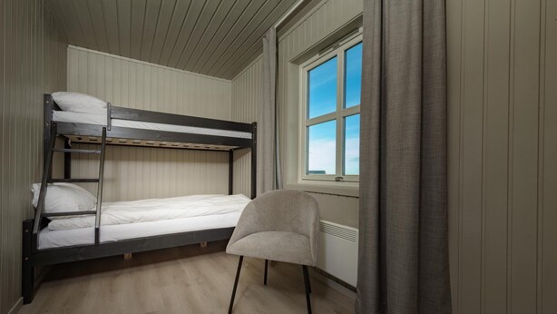 Une chambre avec un lit superposé, une fenêtre et une chaise.