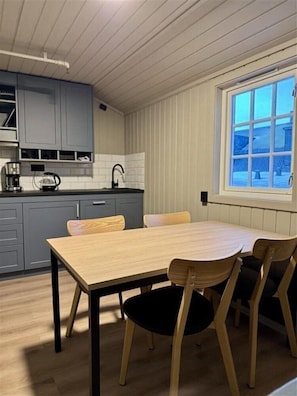 Une cuisine de taille réduite avec des meubles gris, une table à manger en bois et une fenêtre donnant sur un paysage enneigé.