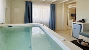 A modern hotel room with a large bathtub, a small kitchenette, and a dining area. - Arlene (Santorini)