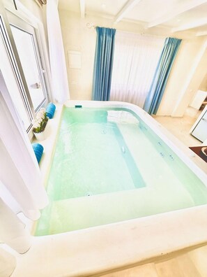Un bain à remous rectangulaire, de couleur vert clair à l’intérieur, entouré de murs blancs et doté d’une fenêtre ornée de rideaux bleus.