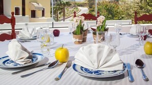 A table set for two with white napkins, blue and white plates, and silver cutlery. There are two yellow apples and two vases with flowers on the table. - Arlene (Santorini)