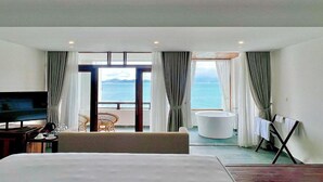 Habitació d'hotel amb llit, televisió, balcó i vistes al mar, banyera i una cadira.
