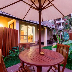 A patio with a round wooden table and chairs, an umbrella, and a view of a building with a tiled roof and a glass door. - Bali Hotel (Phnom Penh)