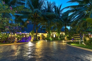 A paved walkway leading to a building with a tiled roof, surrounded by palm trees and tropical plants. - Bali Hotel (Phnom Penh)