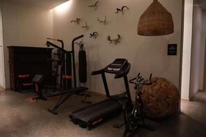 Une salle de sport à domicile équipée de matériel d’exercice, d’une cheminée et de crânes d’animaux fixés au mur.