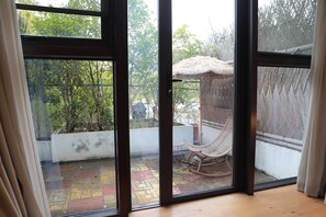 Une pièce dotée de grandes portes vitrées donnant sur un espace extérieur agrémenté d’une structure à toit de chaume et d’un fauteuil en osier.