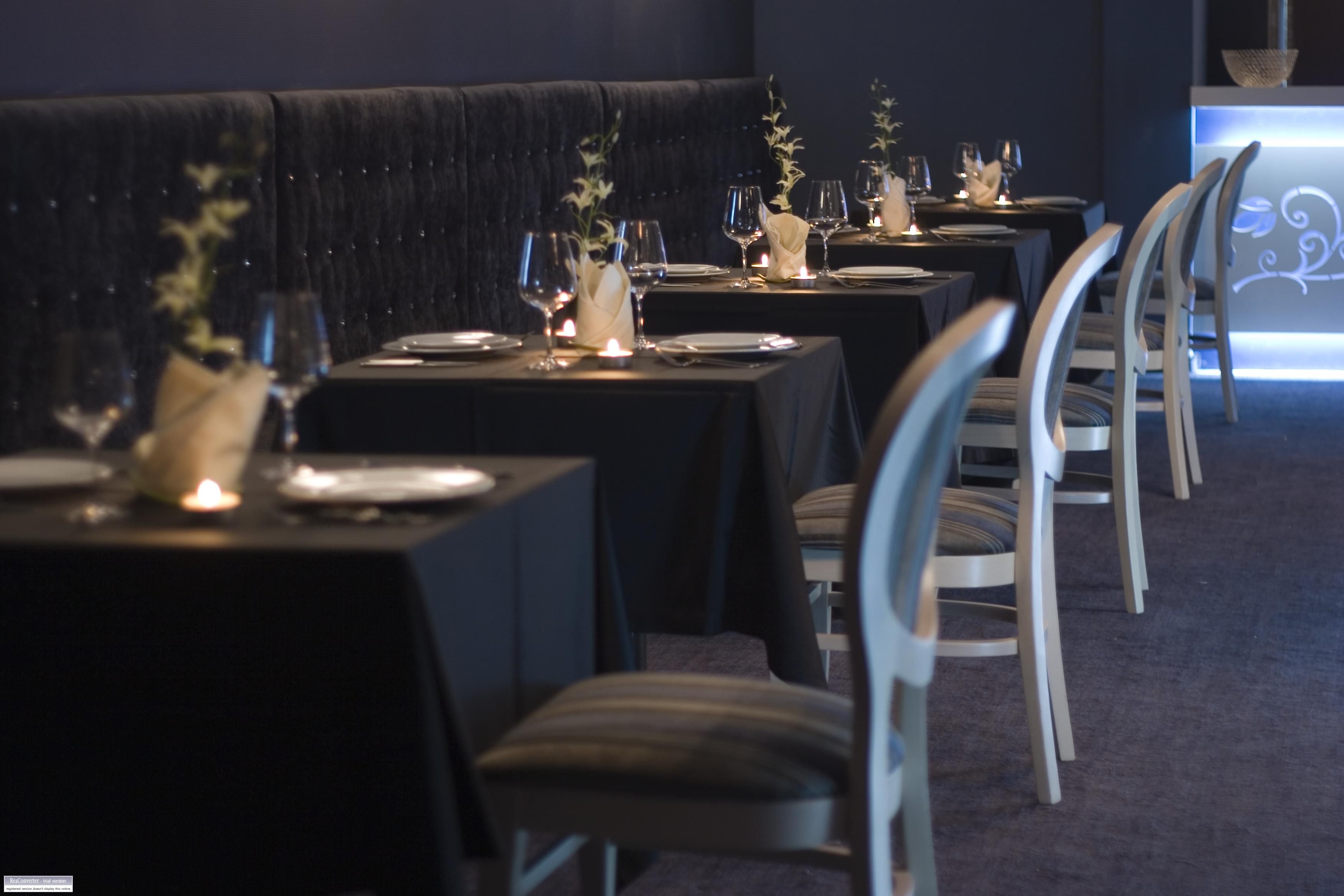 A restaurant with dark velvet booths and tables set with candles, glasses, and plates.