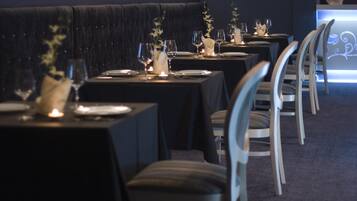 A restaurant with dark velvet booths and tables set with candles, glasses, and plates.