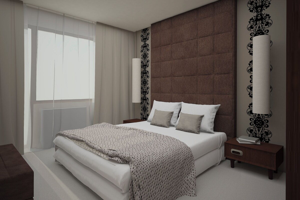 A modern bedroom with a large bed, a nightstand, a bedside table, and a window with sheer curtains.