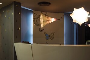 A modern bathroom with a decorative wall featuring butterfly motifs and a unique ceiling light fixture. - Ores Boutique Hotel (Bansko)